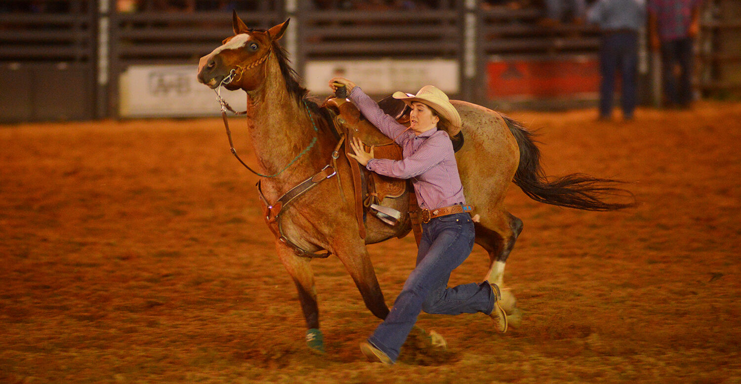 Maci Allison runs with her horse as she jumps off to tie her goat